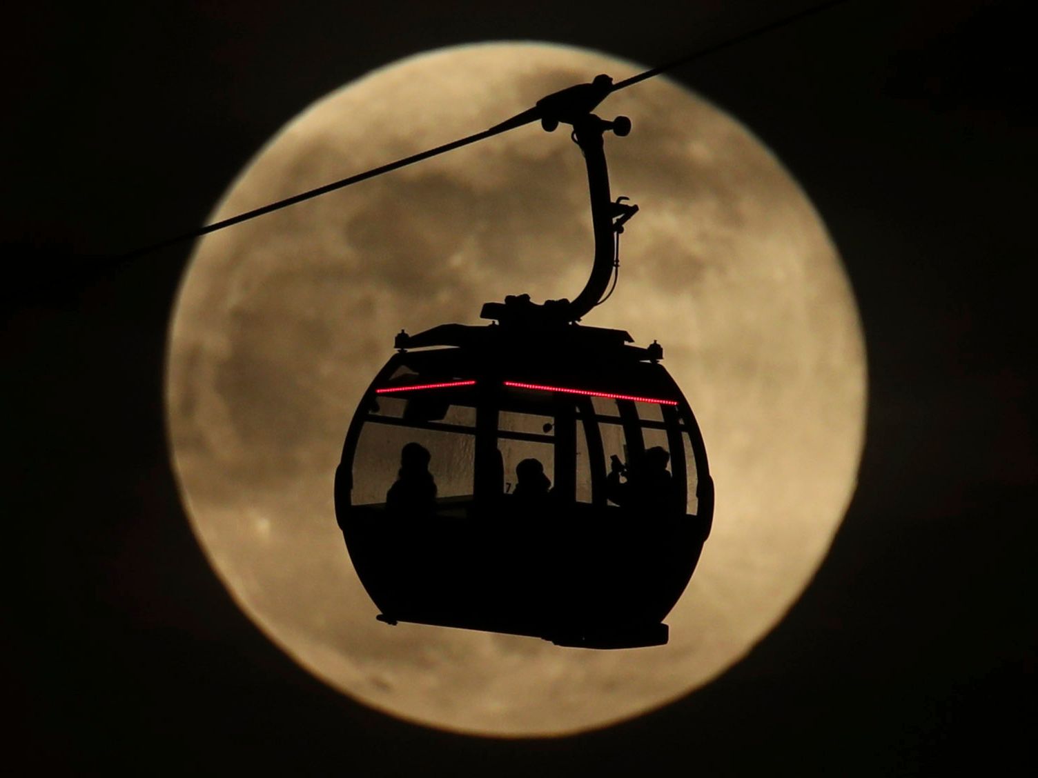 An Emirates Air Line cable cars is silhouetted against the backdrop of the supermoon in Greenwich, London on Feb. 19, 2019. On Tuesday, the moon will "only" be about 221,000 miles from Earth, which is about 17,000 miles closer than average.