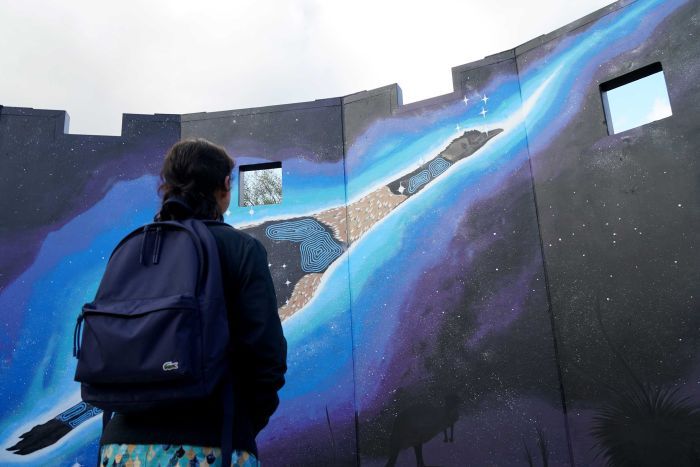 A child looks at a painted mural of an emu.