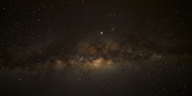 Starry sky with horizontal fuzzy light band and large glowing dot.