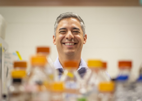 A man peers at the camera from behind a shelf holding glass containers