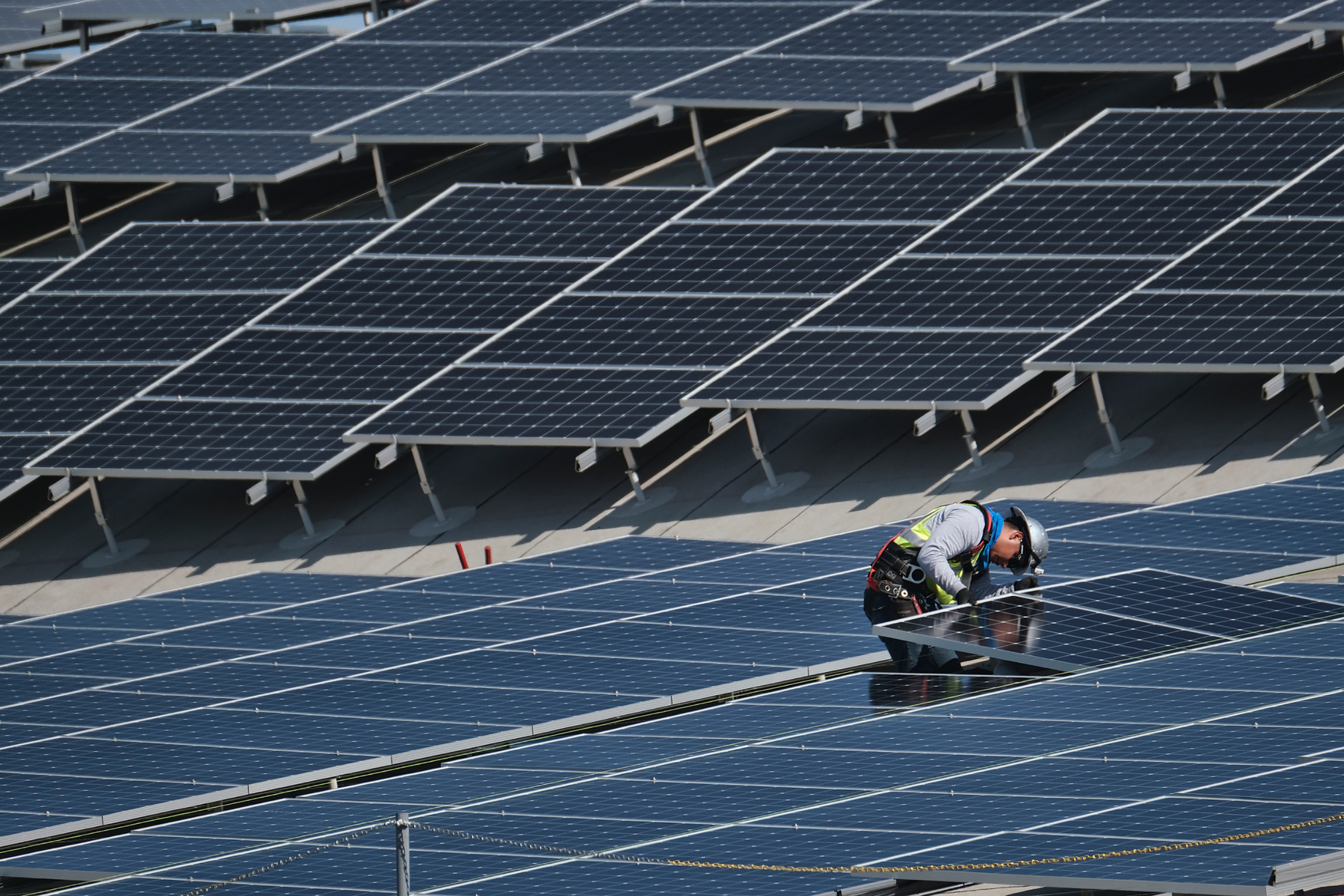 In this Aug. 8, 2019 photo a worker helps to install solar panels onto a roof at the Van Nuys Airport in the Van Nuys section of Los Angeles.