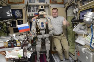 Russia's Skybot F-850 humanoid robot holds a Russian flag with cosmonaut Alexey Ovchinin for a photo in the Zvezda service module of the International Space Station in this photo released Sept. 