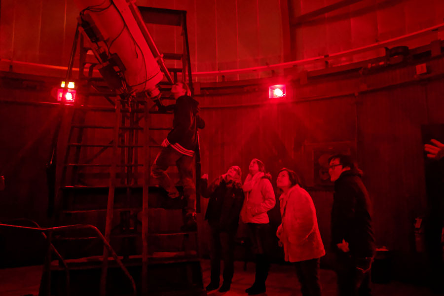 People stand in line under the red glow of the Dearborn Observatory to look through a telescope at the moon on Friday during the CIERA Astronomer Evening. Attendees could also attend a lecture by different researchers about their work in astronomical fields.