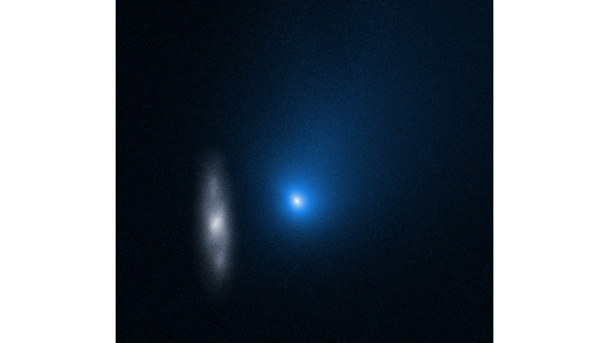 The comet appears as a glowing blue dot in this hubble space telescope image. To the left of it, is a spiral galaxy.