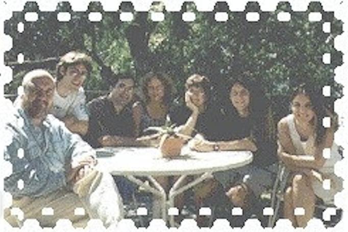 A group of people sitting outside, around a round table.