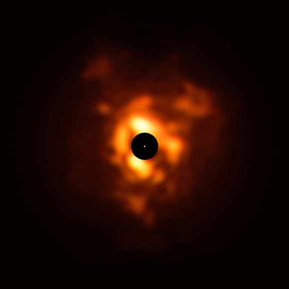 This image, obtained with the VISIR instrument on ESO’s Very Large Telescope, shows the infrared light being emitted by the dust surrounding Betelgeuse in December 2019. The clouds of dust, which resemble flames in this dramatic image, are formed when the star sheds its material back into space. The black disk obscures the star’s center and much of its surroundings, which are very bright and must be masked to allow the fainter dust plumes to be seen. The orange dot in the middle is the SPHERE image of Betelgeuse’s surface, which has a size close to that of Jupiter’s orbit. Image credit: ESO / P. Kervella / M. Montargès et al / Eric Pantin.