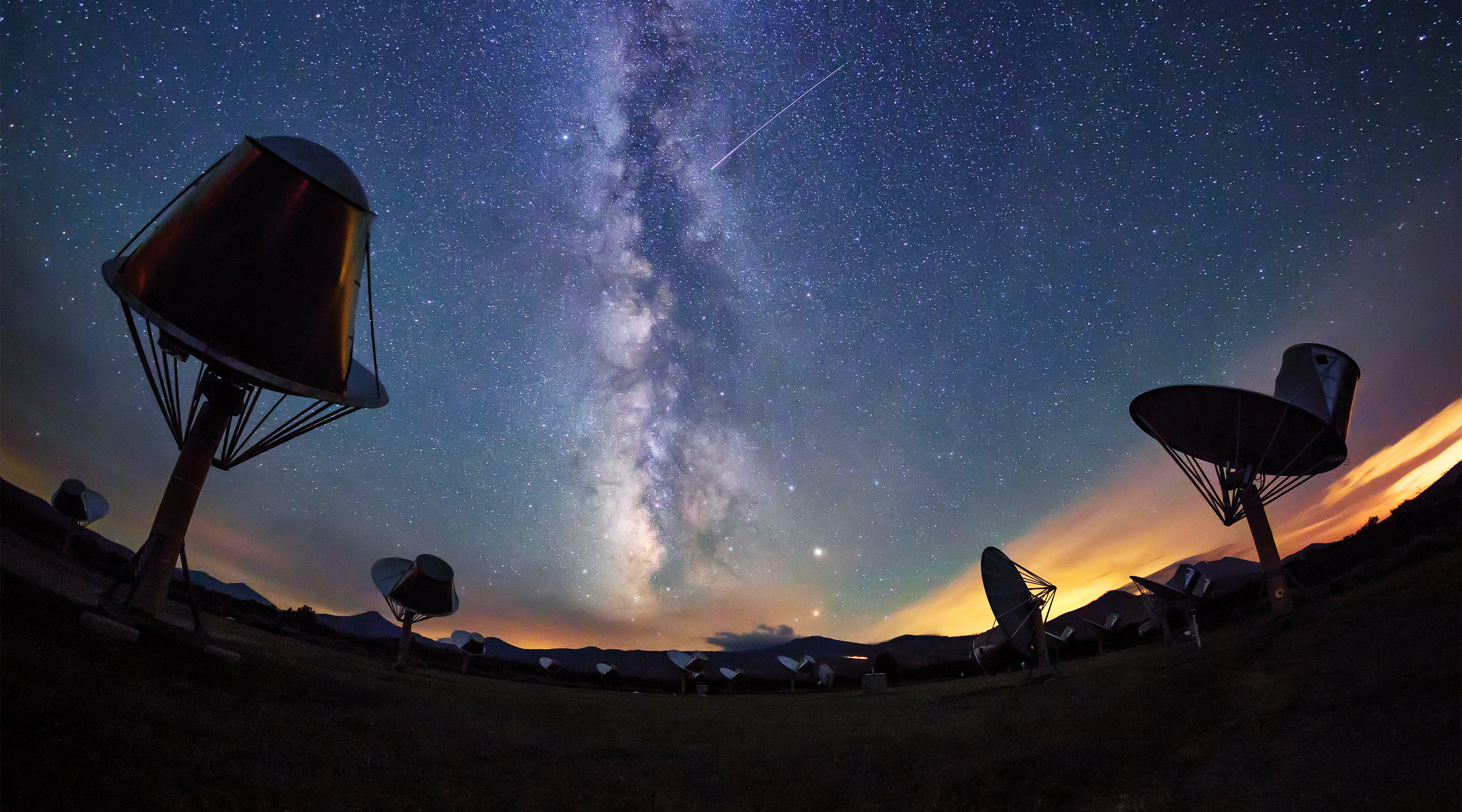 Photo of radio telescopes at the Allen Telescope Array with a starry sky featuring the Milky Way in the background.