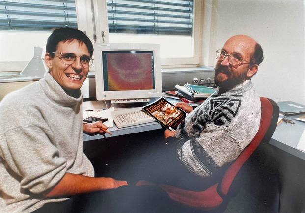 Didier Queloz and Michel Mayor sit in front of a ’90s-era computer; Mayor is holding an issue of the journal Nature.